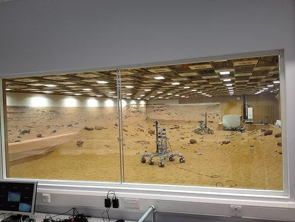 Mars Rover Control Room Internal view of a specialist testing laboratory featuring a Mars simulation environment with rover testing area and controlled observation room