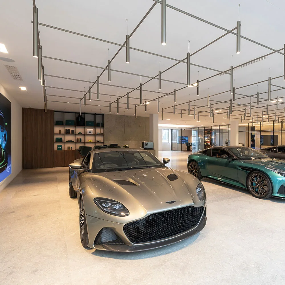 Interior of a luxury Aston Martin showroom displaying high-performance vehicles under modern architectural lighting.