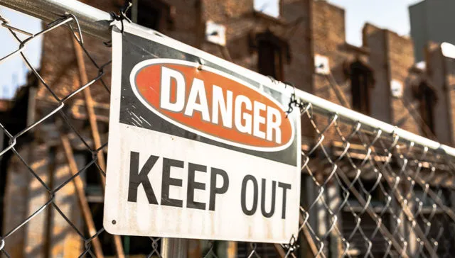 Danger Keep Out warning sign attached to fencing in front of a construction or demolition site.