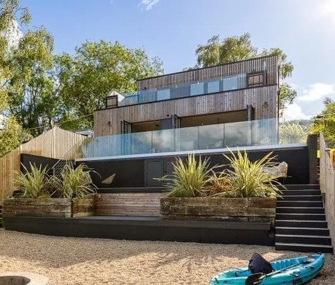 Modern contemporary house with timber cladding, large glass balcony and landscaped garden terrace viewed from the waterfront in Wootton Basset, Isle of Wight