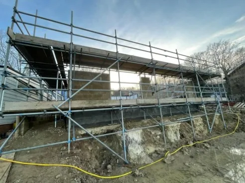 Building construction works in progress with scaffolded structure and foundation groundworks, illustrating residential development during early construction phase
