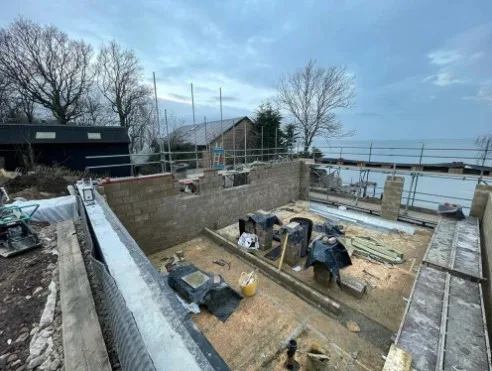 Residential construction project showing blockwork walls, foundations and structural build phase with materials on site, illustrating ongoing building work