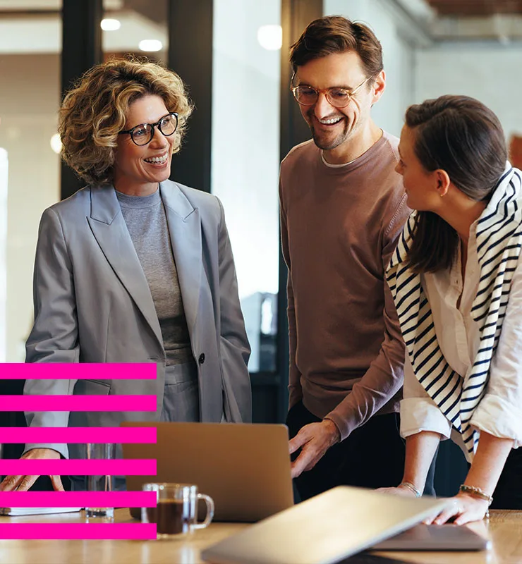 about-us-1resp-image-shape-overlay-new Three professionals collaborating around a laptop in an office meeting, discussing work in a modern workplace setting.