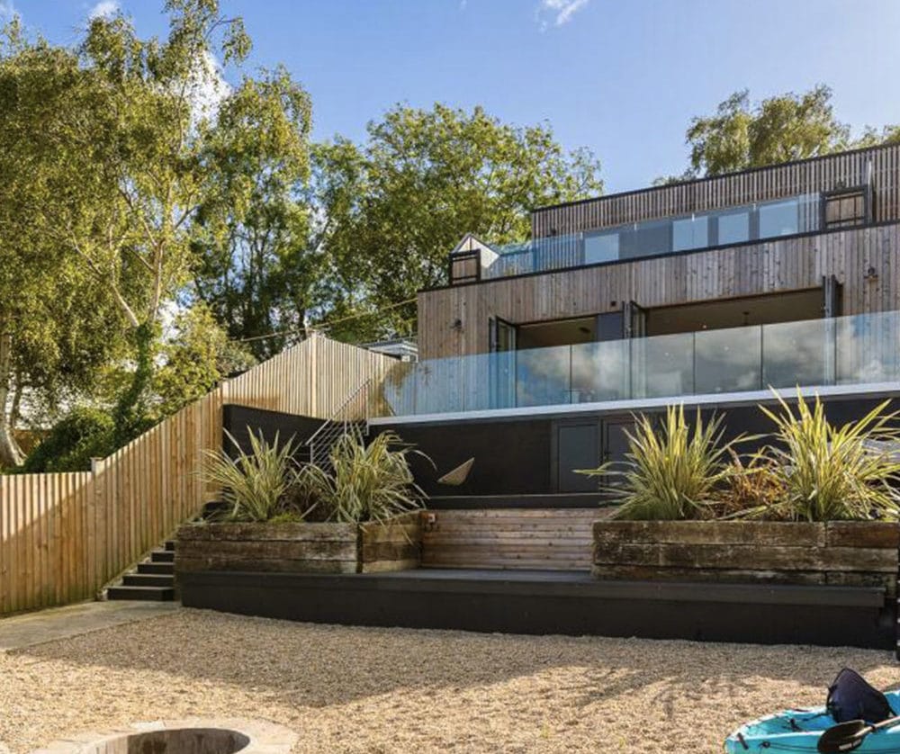 Modern contemporary house with timber cladding, large glass balcony and landscaped garden terrace viewed from the waterfront in Wootton Basset, Isle of Wight