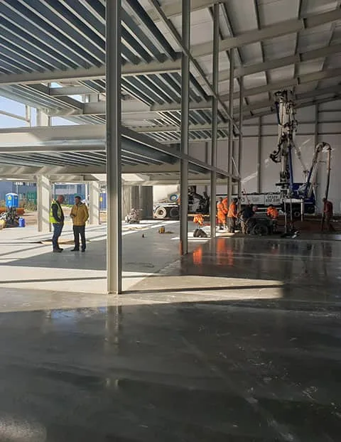 Industrial building construction showing steel frame structure, site operatives and concrete floor installation works in progress within a commercial development