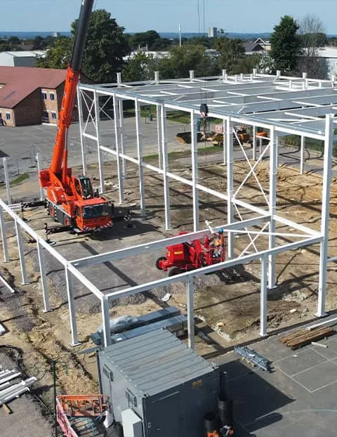Drone aerial photograph of steel frame erection during industrial building construction, showing crane operations and structural installation on a commercial development site