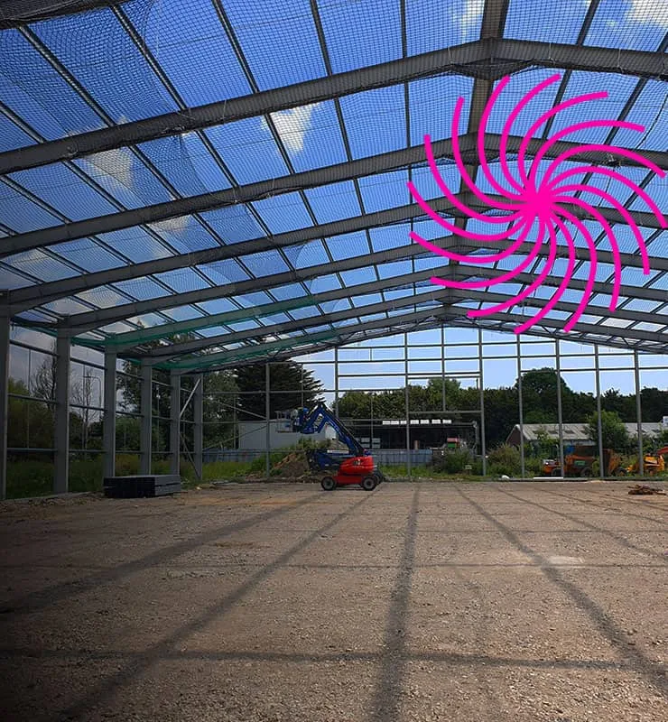 Industrial steel frame building during construction phase showing structural framework, roof installation and on-site access equipment within a commercial development.