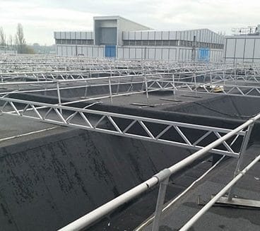 Large flat industrial roof area with access walkways, metal guardrails and rooftop plant structures on a commercial building.