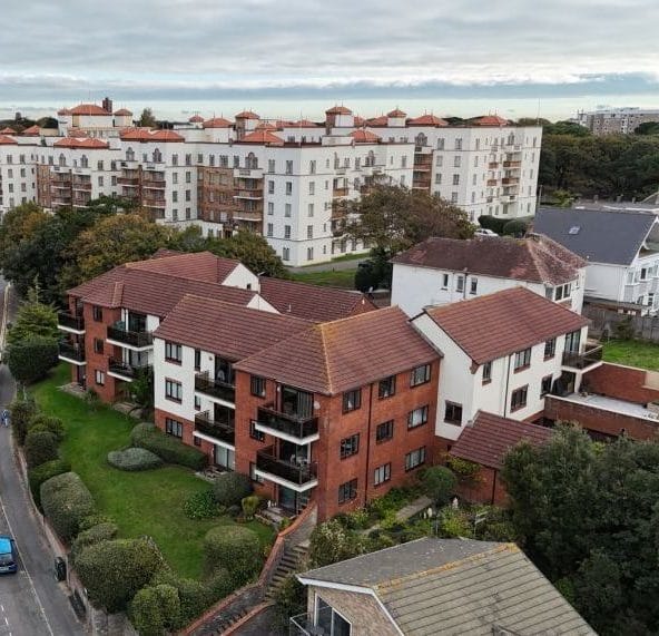 Drone aerial photograph of multi-storey residential apartment blocks and neighbouring housing, showing building layout and external condition within a coastal development Boscombe Dorset