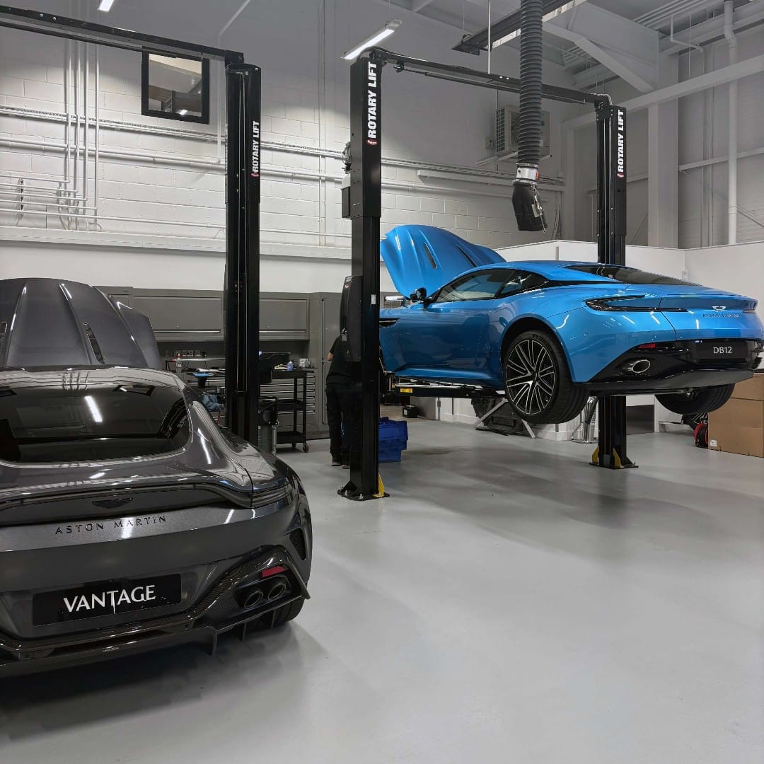 Interior of a high-end automotive workshop with Aston Martin vehicles on hydraulic lifts undergoing servicing and maintenance