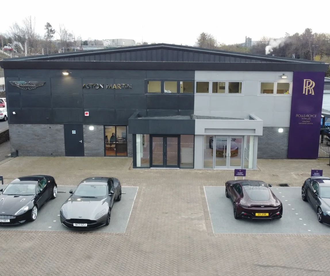 Aerial view of a brand new Aston Martin car dealership with showroom building, forecourt parking and surrounding commercial premises.