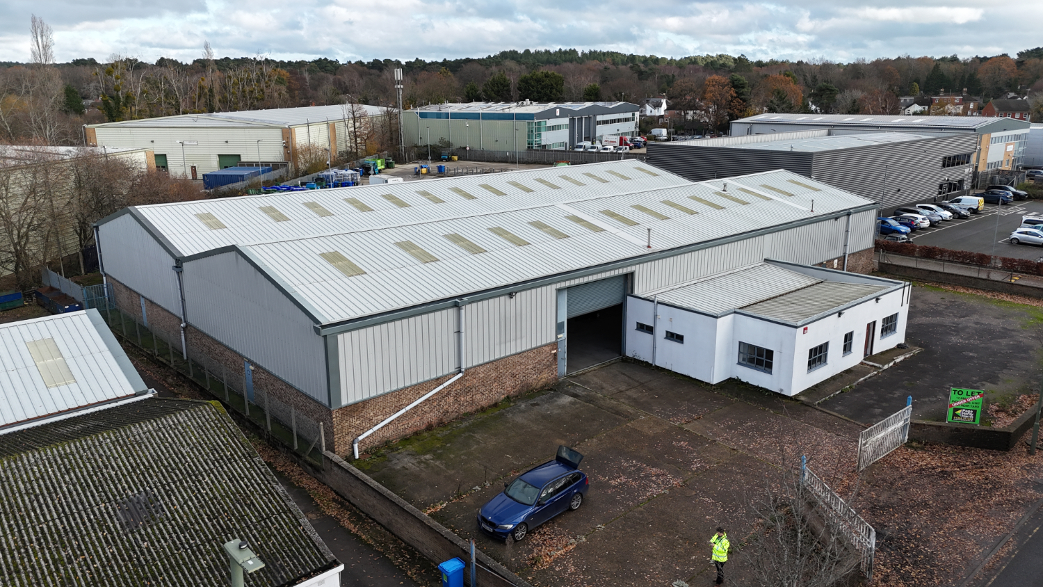 Aerial drone photograph of an industrial warehouse and office unit on a commercial business park in Aldershot Hampshire, showing roof condition, loading access and external yard for property survey and consultancy purposes