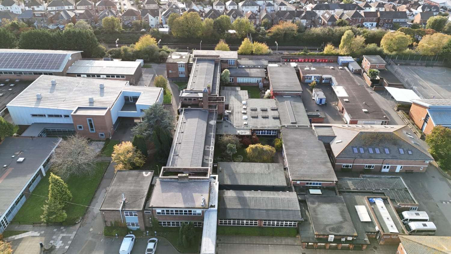 Aerial drone view of school campus building in Poole Dorset and surrounding residential area showing roof layouts and site condition