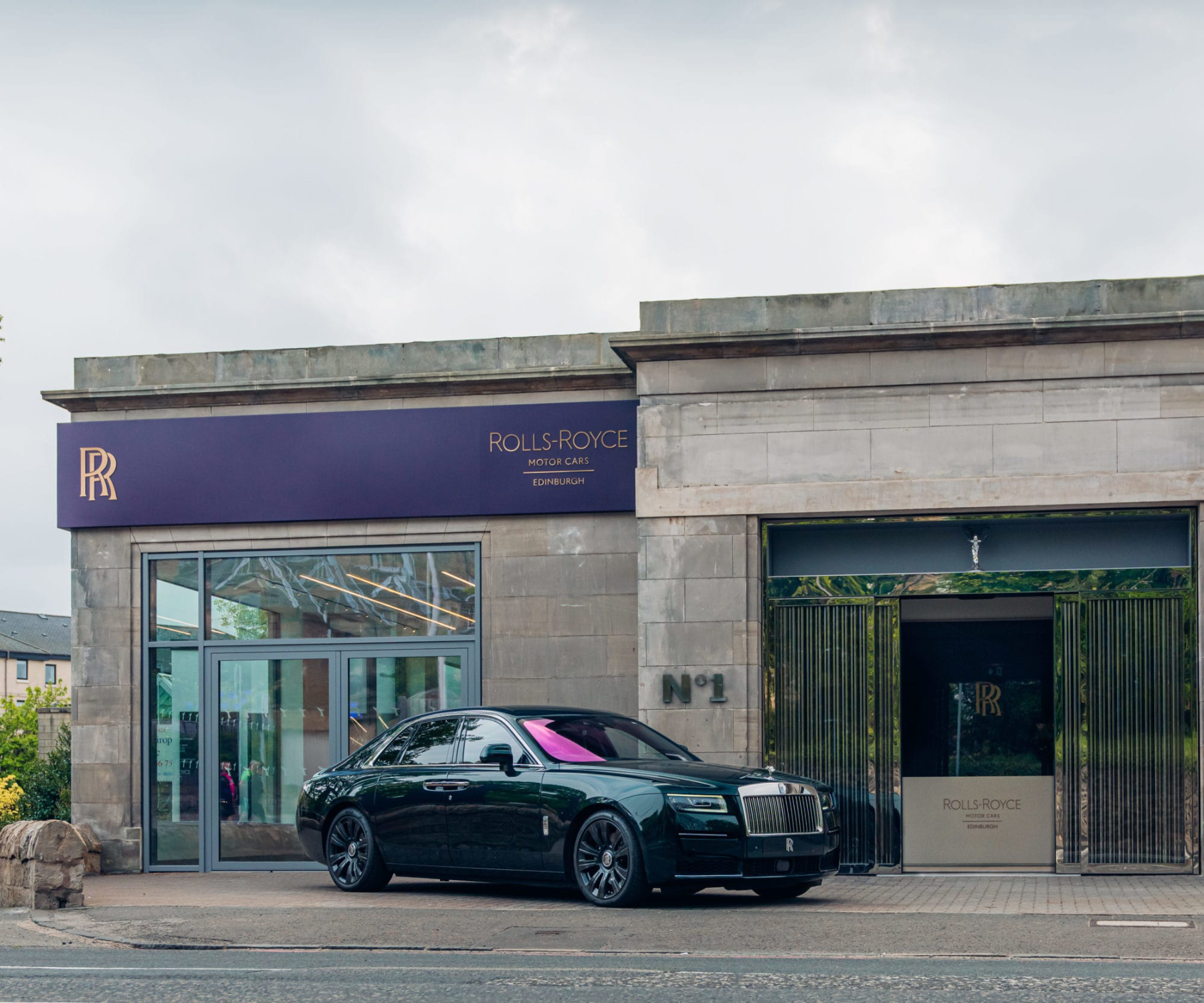 External image of a Rolls-Royce car displayed outside a modern dealership showroom interior with premium retail fit-out and display area